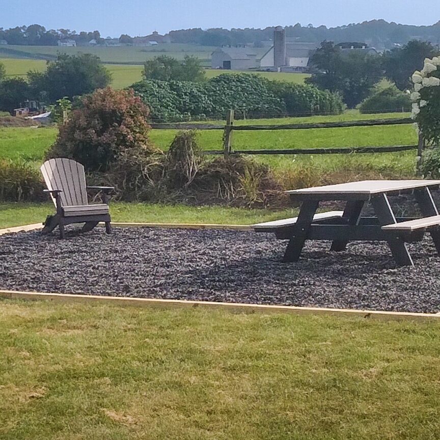 A gravel patio area for a fire pit with chairs and a picnic table